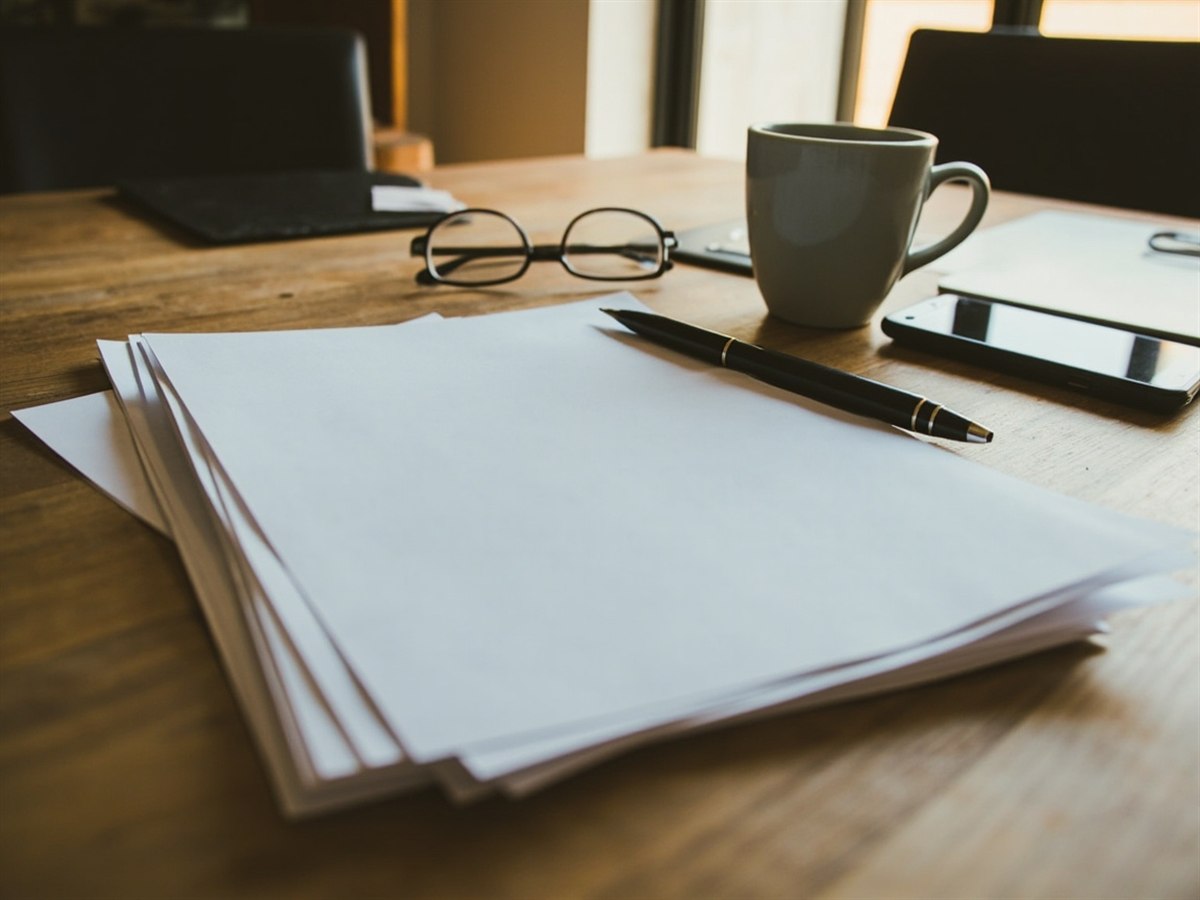 A printed health insurance plan opened on a kitchen table, half read, a coffee cup beside it.