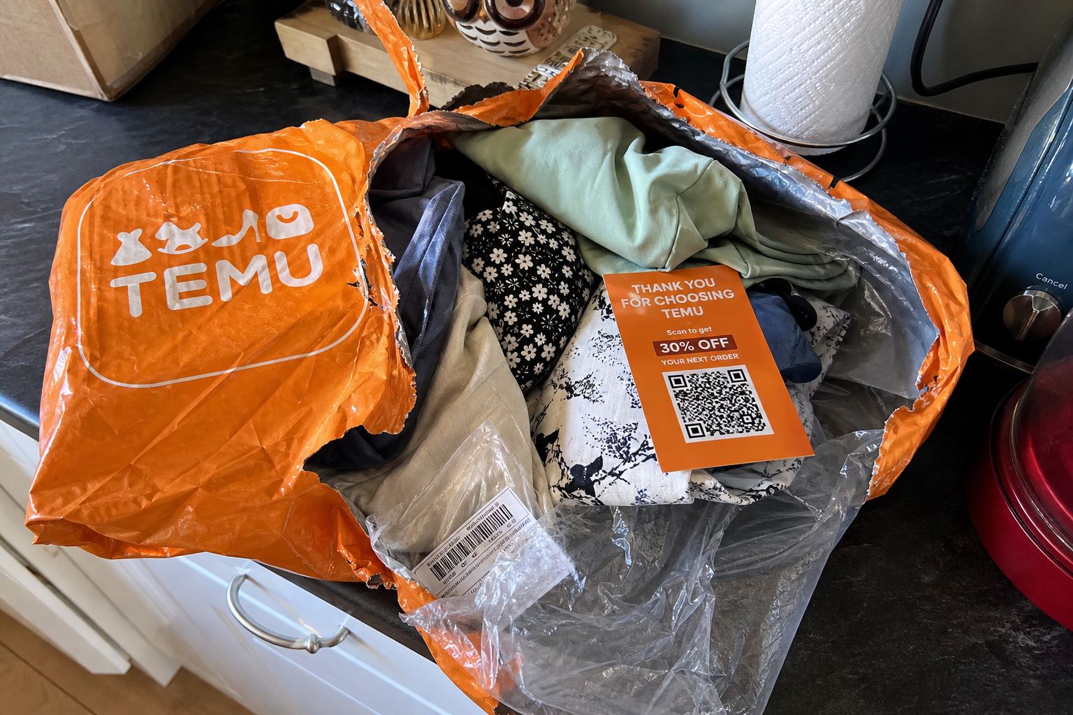 An unordered Temu mailer ripped open, cheap clothes and a QR card inside.